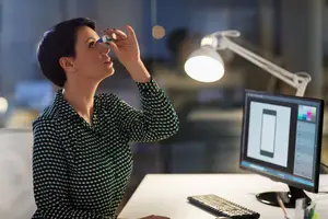 A woman is using a nasal spray while sitting at her desk in the office