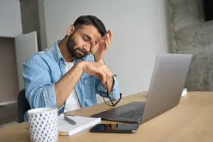Tired man rubbing his eyes while looking at a laptop screen
