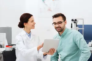 A woman doctor in white coat and a man in eyeglasses looking at a tablet in an office