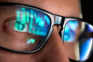 Close up of a persons face with glasses and green and blue lights reflecting in them