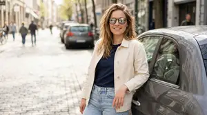 A woman leaning against a parked car on a city street with cars and people in the background