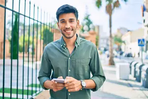 A man in a green long-sleeve shirt smiling while holding a cell phone in his hands