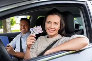 A woman holding her driver's license in the driver's seat of a car