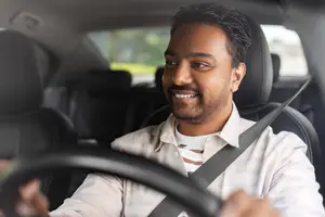 A man smiling while driving a car with his seat belt on