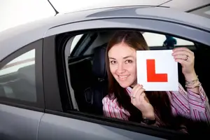 A young woman with an L plate is sitting in a car, smiling and posing for a photo.