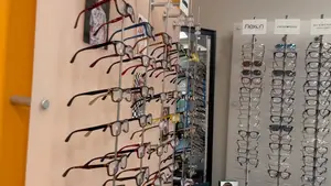 A display of eyeglasses on racks against a wall, with signs and a picture in the background