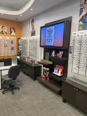 A room with an empty desk, a chair, a monitor, and a rack with many glasses hanging on the wall