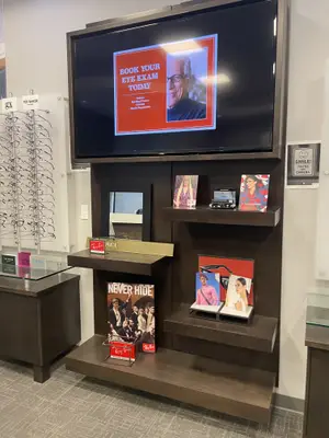 A display of eyewear products in a store with a television monitor displaying an advertisement for booking an eye exam