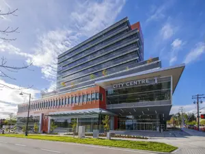 A high-rise building with the text City Centre is on the side of the road with a grassy field in front of it.