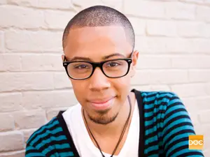 A man wearing a striped shirt and glasses is smiling and posing for a photo