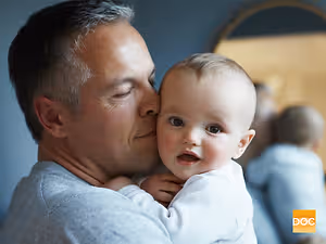 A man holding a baby with a blurry background in a room