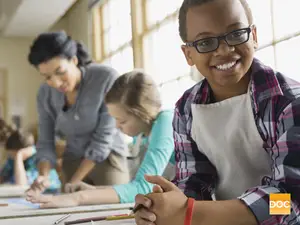 A group of students are sitting at a desk with pencils and papers in a classroom.