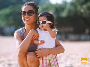 A woman and a young child wearing sunglasses on a beach.
