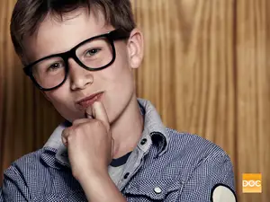 A young boy wearing glasses and a checkered shirt is posing for a picture.