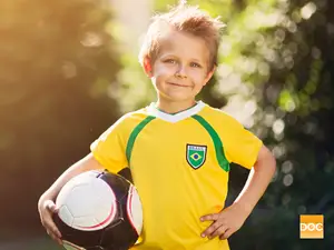 A young boy wearing a Brazilian soccer jersey smiles and holds a soccer ball.