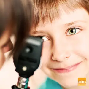 A young boy with green eyes is having his eyes examined with an ophthalmoscope.