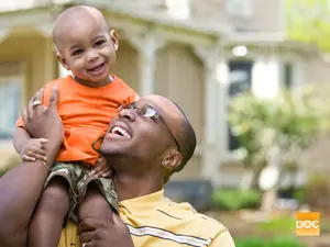 Man in glasses holding a child in front of a house
