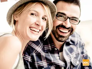 A smiling couple, a woman wearing a hat and a man with glasses, posing for a photo.
