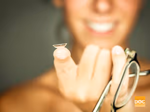 A woman holds a contact lens and a pair of glasses in her hands.