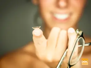 A woman holds a contact lens and a pair of glasses in her hands.
