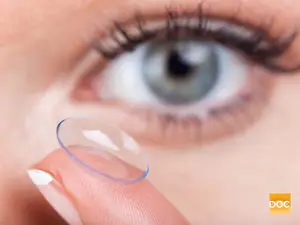 A woman's eye with a contact lens being held by a fingertip.