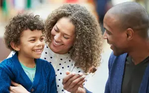 An African American family sitting together, the woman smiling at the child while the father holds a fork with cake on it