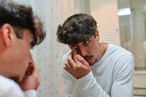 A man is looking at his nose in the mirror and touching it with his finger.