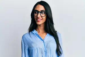 A smiling woman wearing glasses and a blue shirt poses against a white background