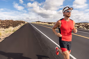 A male runner is running on a road under the blue sky with white clouds