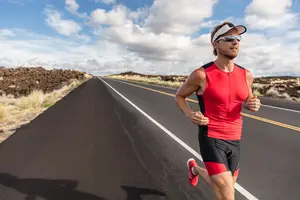 A male runner is running on a road under the blue sky with white clouds