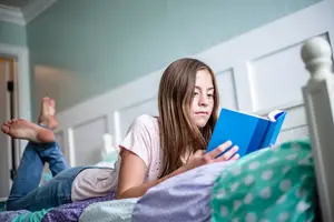 A girl lying on the bed reading a blue book