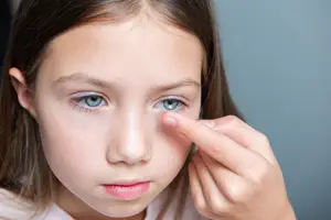 A girl with blue eyes trying to put in a contact lens