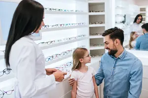 A man and a girl are standing in front of a woman with a child, all in front of a shelf filled with glasses in a store.