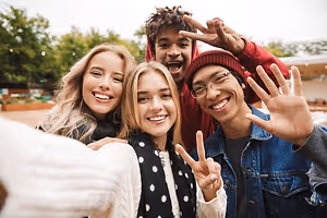 Group of friends making peace signs and smiling for a selfie in a park