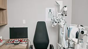 An image of a doctor's room with an ophthalmoscope, a black chair, and an eye chart on the wall.