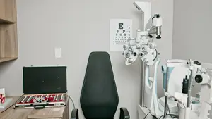 An image of a doctor's room with an ophthalmoscope, a black chair, and an eye chart on the wall.