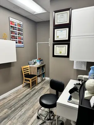 An office with a desk, two chairs, a cabinet, a white board, a framed certificate, a poster, and a bottle on top of a desk with a microscope, a book, and a cabinet with books on the floor