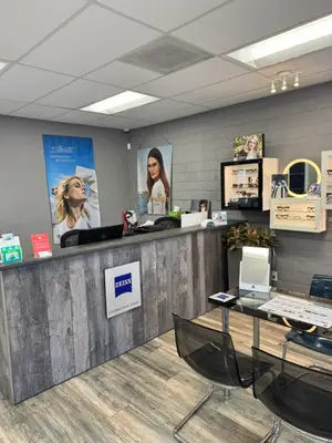 An optical shop with a reception desk, a woman's poster, and a woman in front of the mirror, along with several frames on display.