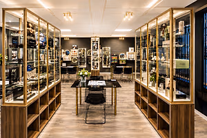 A luxury eyewear store with high-end glasses on display, wooden shelves, and black tables with flowers, with two golden display cases on either side, with a black wall in the background, and lamps on the ceiling.