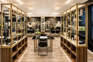 A luxury eyewear store with high-end glasses on display, wooden shelves, and black tables with flowers, with two golden display cases on either side, with a black wall in the background, and lamps on the ceiling.