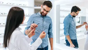 A man and a woman are standing in front of a shelf with many eyeglasses on display in a store