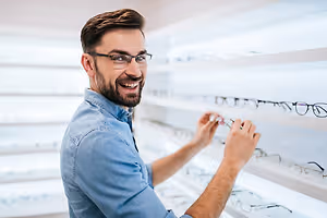 A man is picking out a pair of glasses in a glasses shop.
