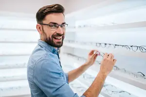 A man is picking out a pair of glasses in a glasses shop.