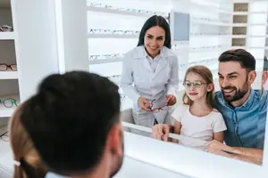 A young girl with glasses is smiling and looking at a man and a woman in front of her.