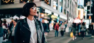 Woman standing in a busy city street, looking up at the lights
