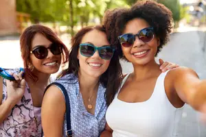 Three women smiling and posing for a selfie while standing on the side of the road