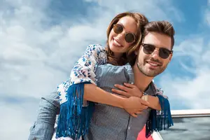 A couple smiling and posing for a photograph with a car in the background