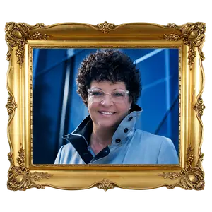 Portrait of a woman with curly hair and glasses wearing a blue jacket and smiling at the camera inside a gold-colored ornate picture frame