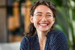 A woman wearing glasses and a polka dot shirt is smiling and seems to be posing for a photo.