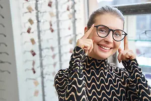 a smiling woman in glasses holding up her fingers in front of her eyes